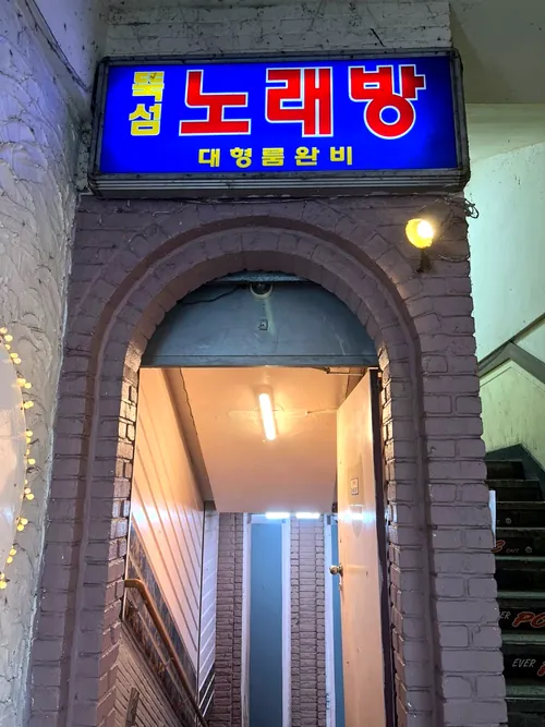 건물 입구 아치 위의 파란 간판 '뚝섬 노래방 대형룸완비'